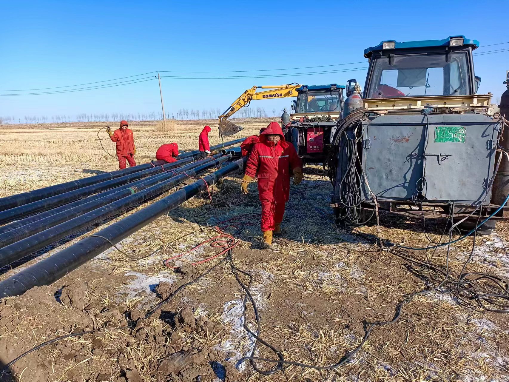 Pipeline construction crew installing coated steel pipe at an oil and gas project site during winter